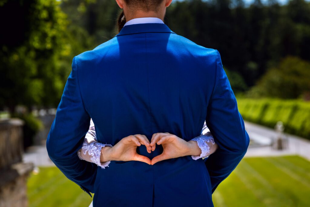 Bride and groom making a heart shape with hands, symbolizing love in an outdoor setting.