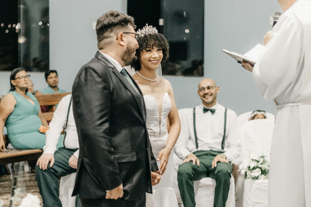 Bride and groom smiling during a wedding ceremony inside a church with guests in attendance.