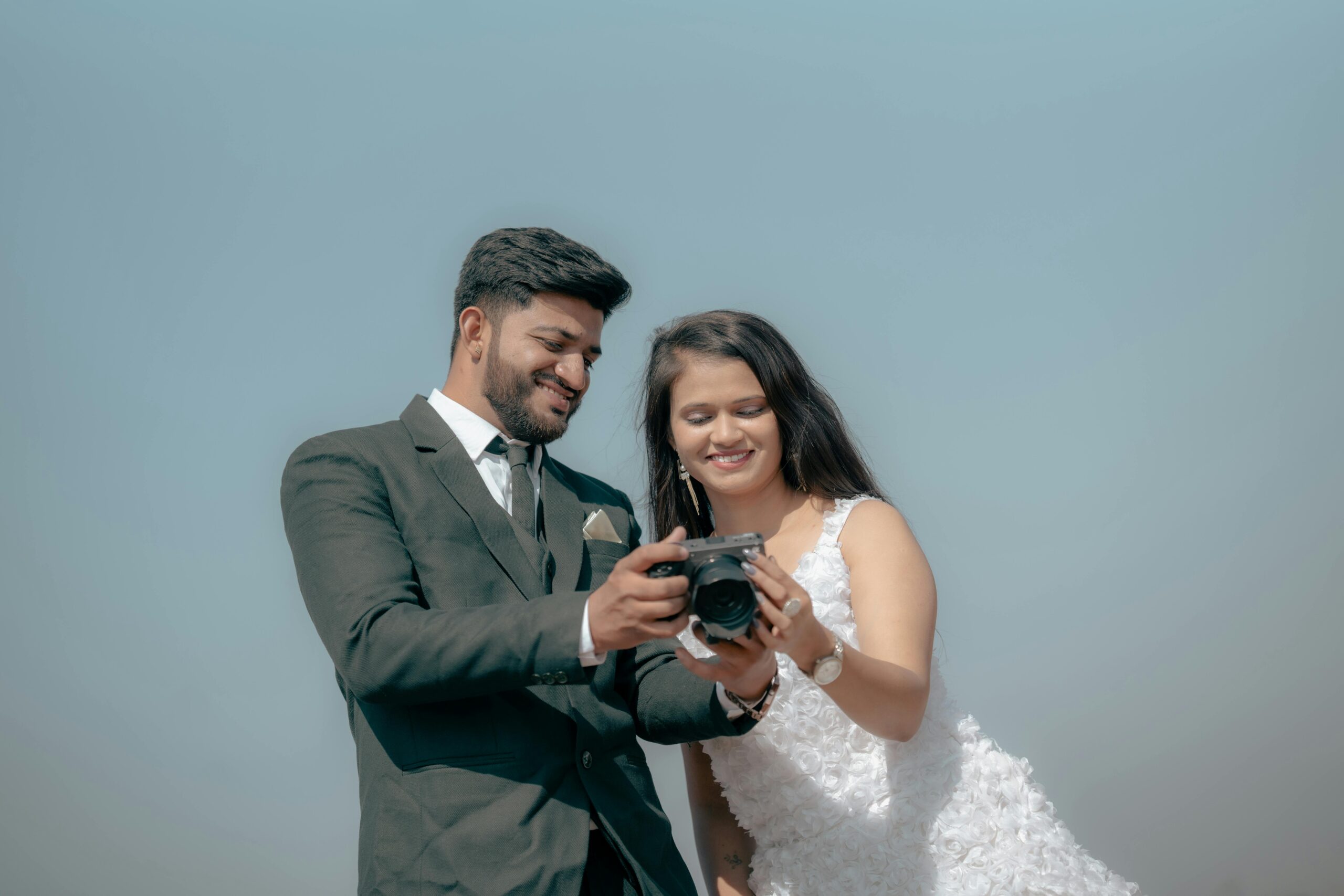 Smiling couple reviewing wedding poses and photos on camera during an outdoor pre-wedding shoot.