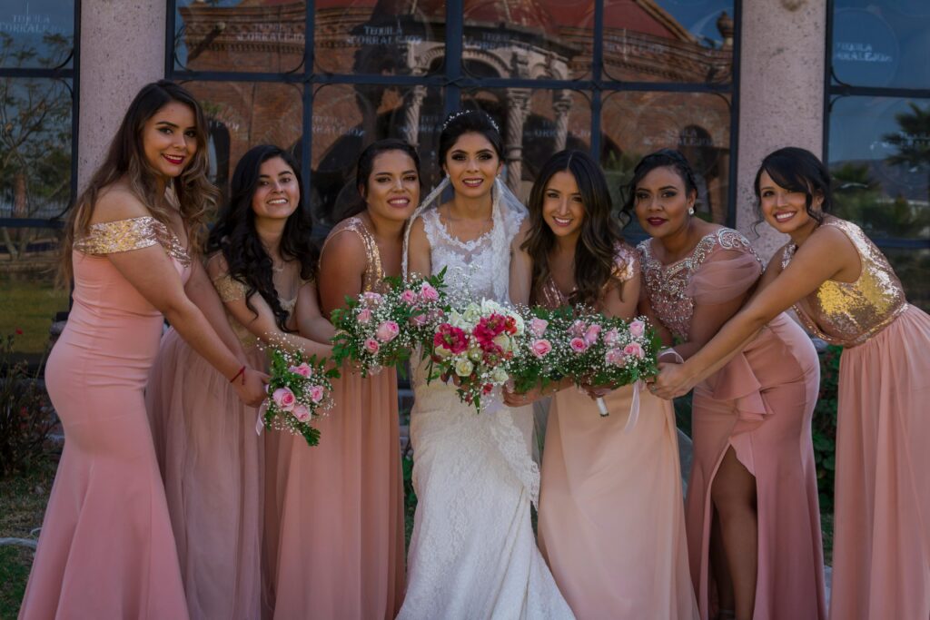 A joyful bride and her bridesmaids posing outdoors with bouquets on a sunny wedding day.