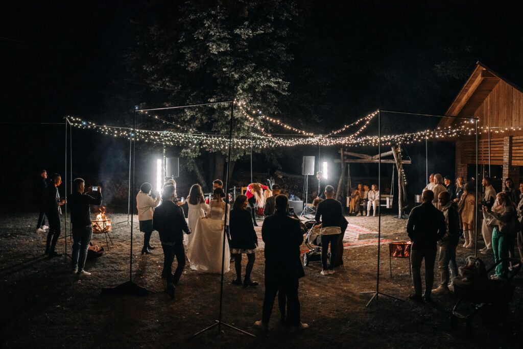 An outdoor wedding reception at night with string lights and guests enjoying the festivities.