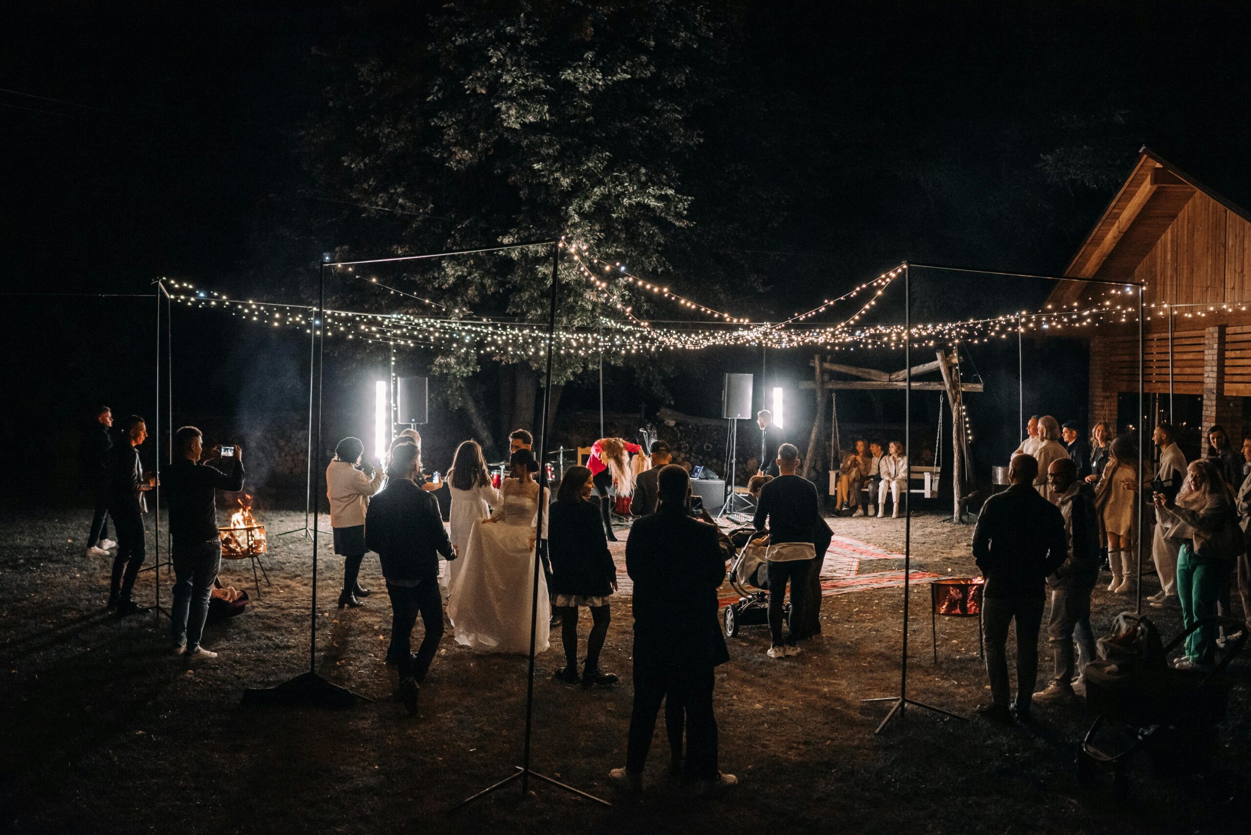 An outdoor wedding reception at night with string lights and guests enjoying the festivities.