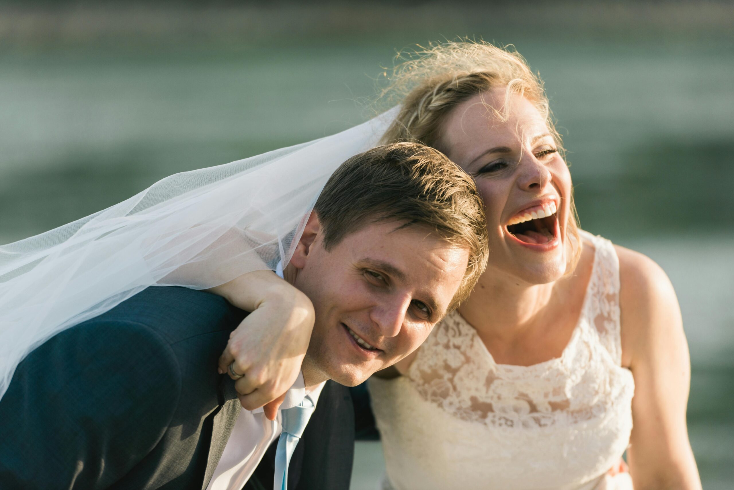 Happy bride and groom laughing together outdoors by the water.