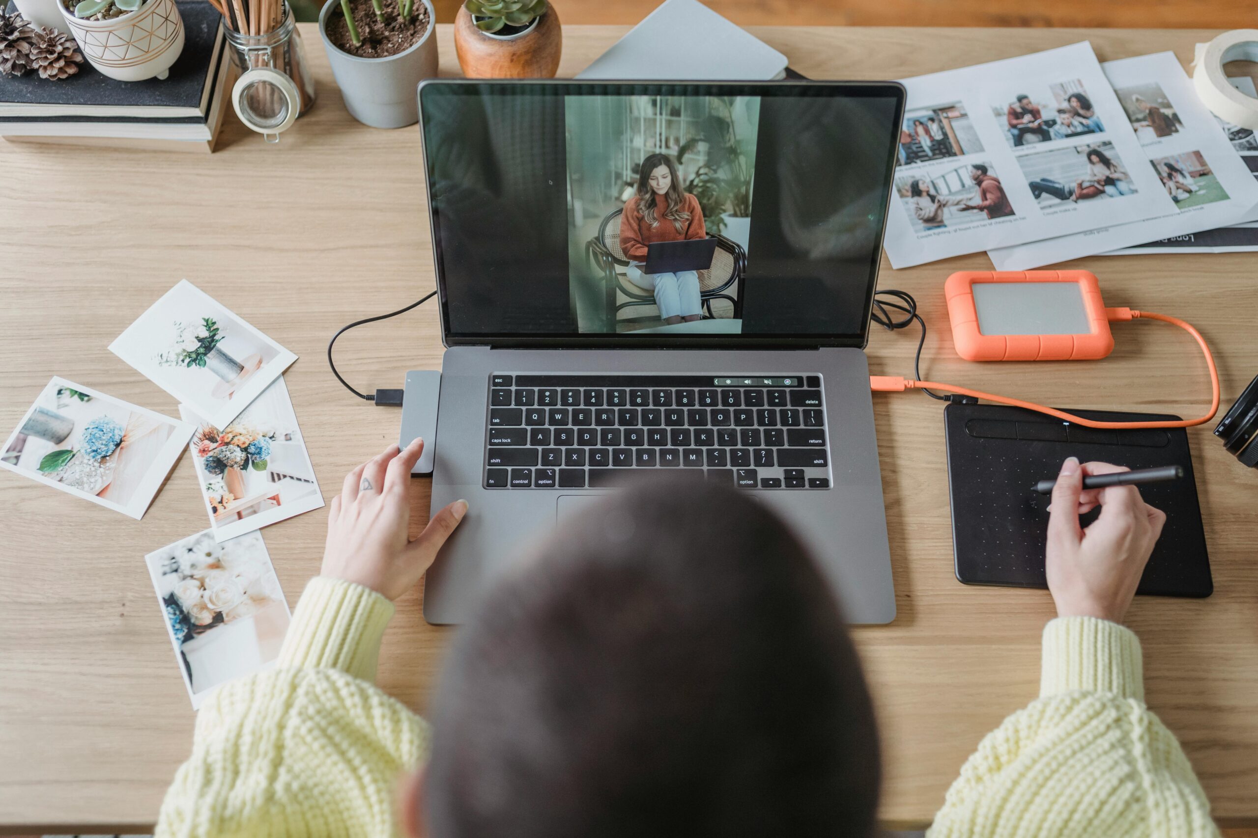 Overhead view of a creative workspace featuring a laptop, tablet, and photo editing accessories.
